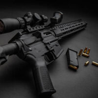 Modern automatic carbine with optical and collimator sight. A rifle with two sights on a dark background. Cartridges for weapons near a carbine.